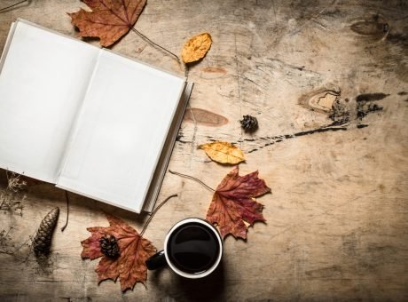 Autumn style. Open book with a hot Cup of coffee. On wooden background.